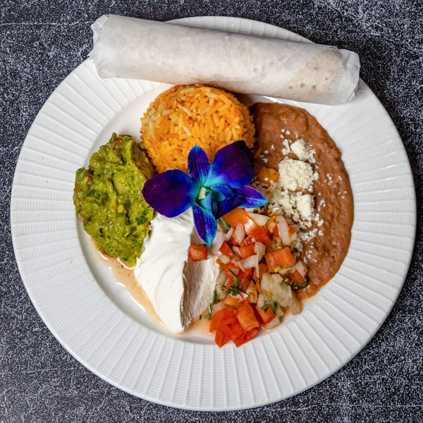 A burrito with rice, refried beans, guacamole, pico de gallo, sour cream, and a blue orchid.
