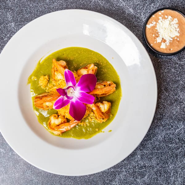 Shrimp in green sauce with rice and a purple orchid, alongside a bowl of refried beans.