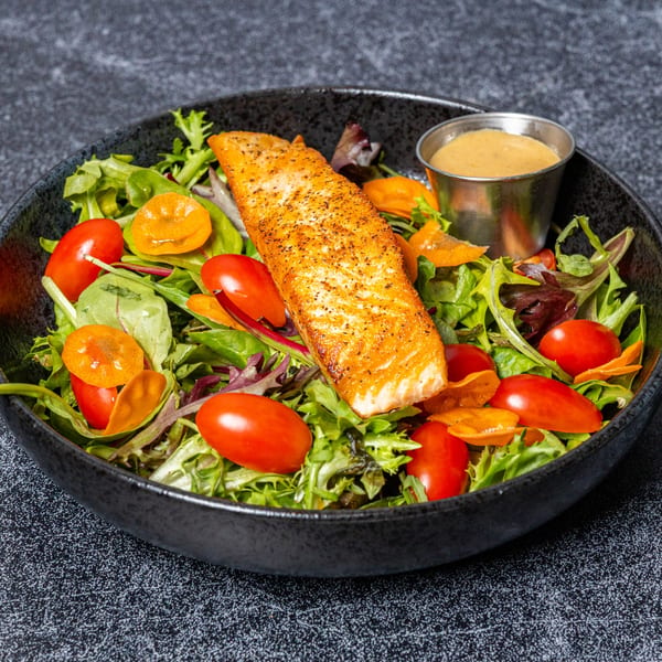 Grilled salmon fillet on a fresh green salad with cherry tomatoes, orange slices, and dressing.